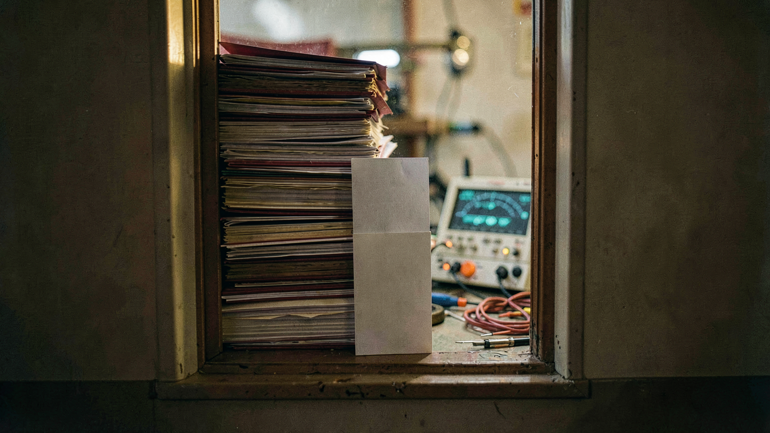 A narrow window frame with a floor-to-ceiling mass of spec folders pressing against it from outside, only three slim folders having passed through to rest on the inside sill.